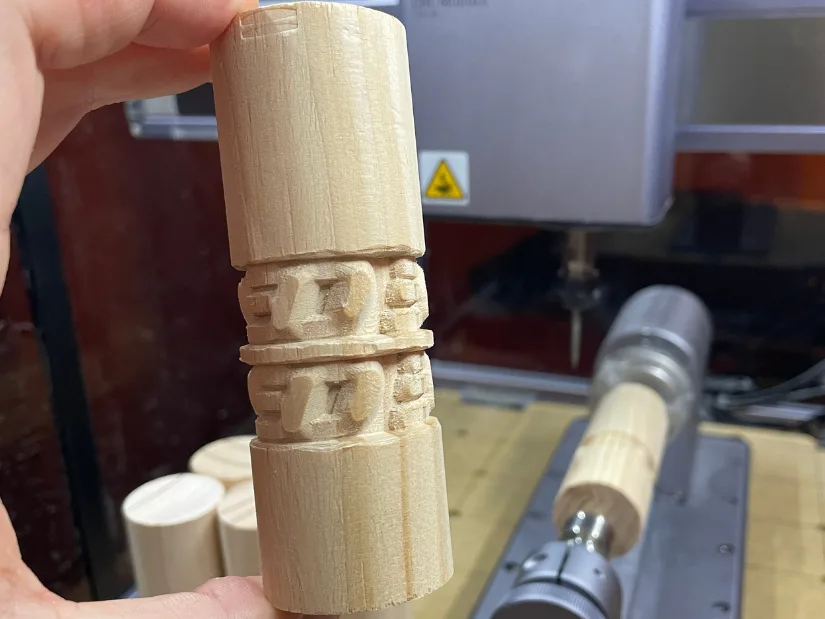 Close-up of a wooden dowel carved with the 性发视频 logo using Snapmaker 4-axis 性变视频 rotary module, showing partial but recognizable results