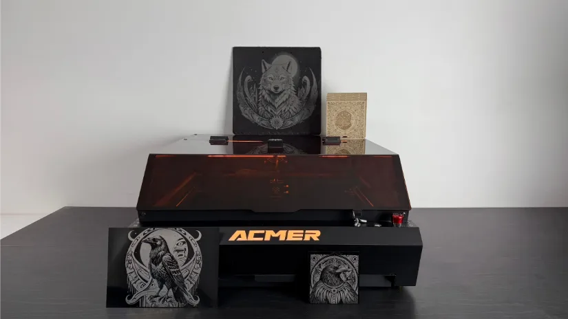  An Acmer P3 24W laser machine with a dark, transparent cover and vibrant orange "ACMER" branding, surrounded by an array of completed projects—including intricate engravings of a wolf, bird, and owl on black materials as well as a detailed beige pattern—demonstrating the machine's precision and craftsmanship.