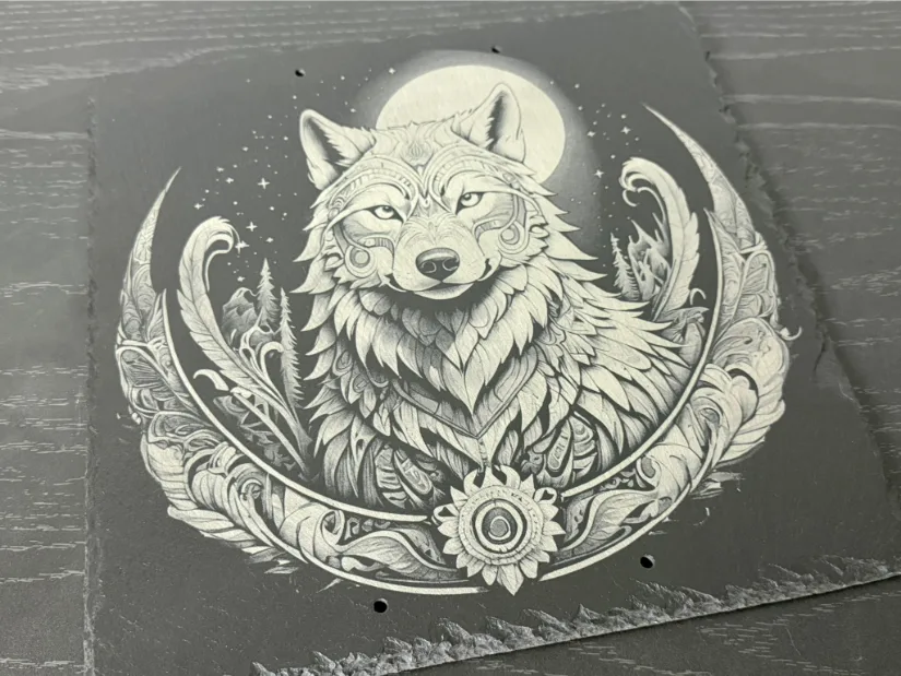  An intricately engraved wolf on a slate surface featuring detailed ornamental patterns, a serene, focused expression, and a circular floral design accented by a full moon and stars.