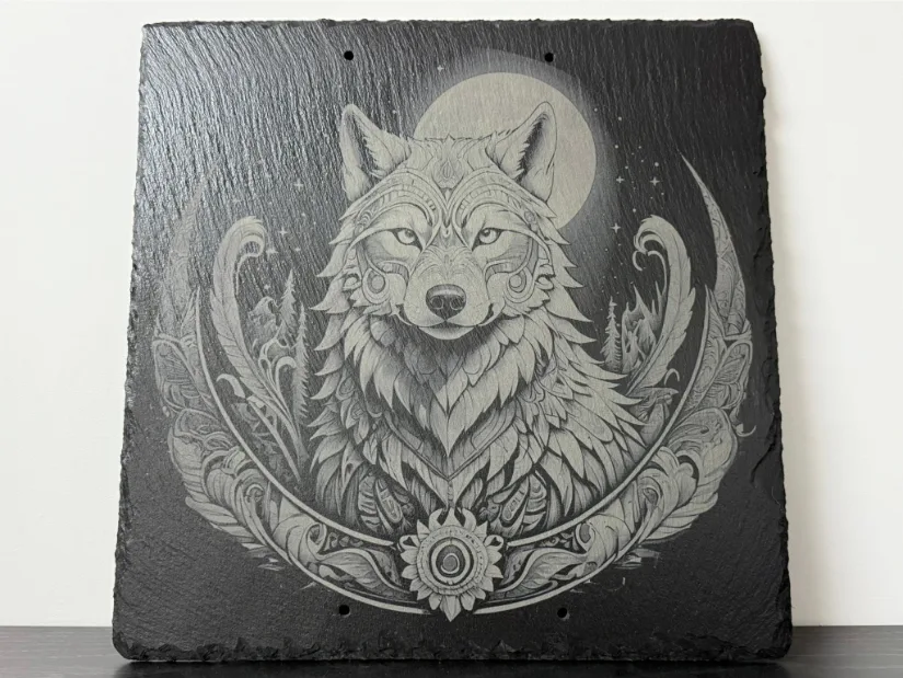  An intricately engraved wolf on a slate surface featuring detailed ornamental patterns, a serene, focused expression, and a circular floral design accented by a full moon and stars.