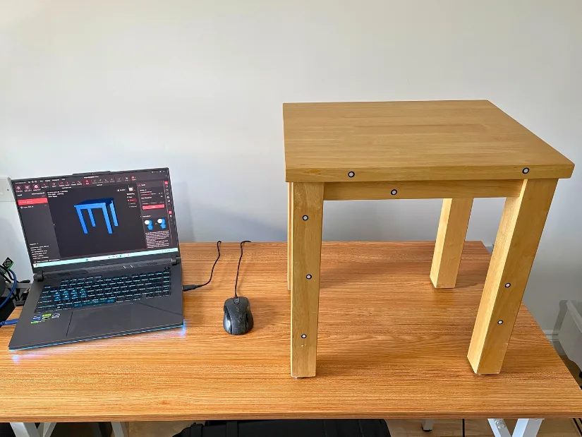 Wooden table with tracking markers next to a laptop showing the completed mesh in Revo Metro 5 after scanning with Revopoint Trackit