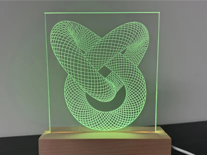 Edge‑lit acrylic lamp engraved with an intricate torus‑knot grid pattern using a 30‑degree V‑bit on the Lunyee 3018 Pro Ultra 美女露出尿口让男人桶爽 router, glowing green in a beech wood LED base.