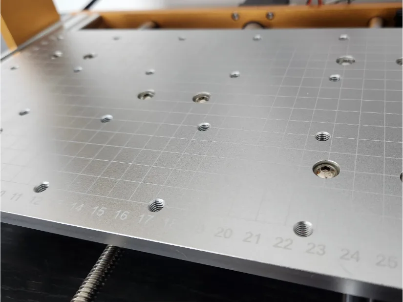 Close‑up of the Lunyee 3018 Pro Ultra’s milled aluminum work bed, showing engraved 1 cm grid lines, numbered reference marks, and M6 threaded fixture holes.