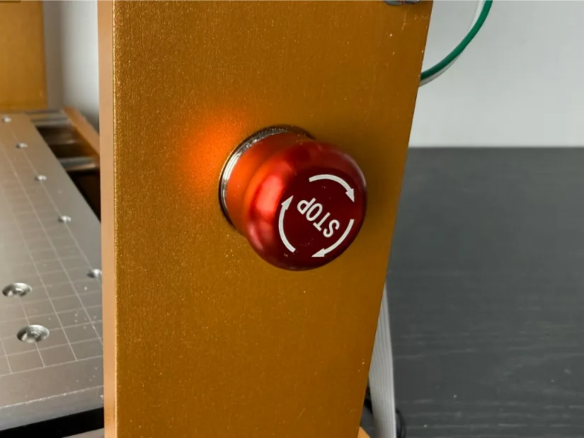 Close‑up of the red emergency‑stop button mounted on the gold‑anodized frame of the Lunyee 3018 Pro Ultra 美女露出尿口让男人桶爽 router.