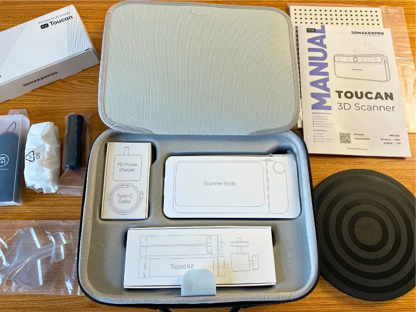 3DMakerpro Toucan accessories laid out, including protective case, scanner body, tripod kit, cables, charger, manual, and scanning mat